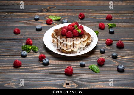 Porzione di tipico dessert tiramisù con lamponi e mirtilli sfondo di legno Foto Stock