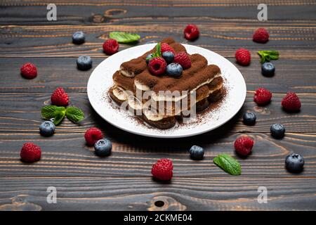 Porzione di tipico dessert tiramisù con lamponi e mirtilli sfondo di legno Foto Stock