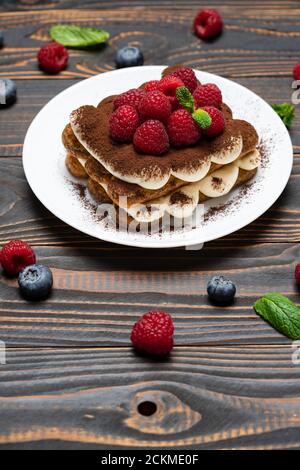 Porzione di tipico dessert tiramisù con lamponi e mirtilli sfondo di legno Foto Stock