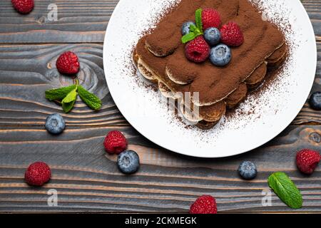 Porzione di tipico dessert tiramisù con lamponi e mirtilli sfondo di legno Foto Stock