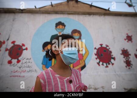 Khanyois, striscia di Gaza, territori palestinesi. 15 settembre 2020. Una ragazza palestinese che indossa una maschera frontale davanti a un murale raffigurante bambini che indossano una maschera facciale dipinta su un muro a Khanyois, nella striscia meridionale di Gaza. Credit: Ahmad Salem/ZUMA Wire/Alamy Live News Foto Stock