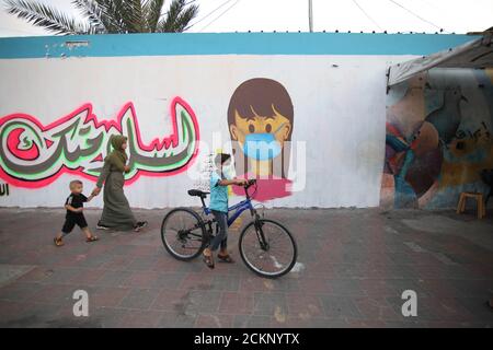 15 settembre 2020, Khanyois, striscia di Gaza, territori palestinesi: Un ragazzo palestinese fa un giro in bicicletta davanti a un murale di consapevolezza del coronavirus a Khanyois, nella striscia di Gaza meridionale. (Immagine di credito: © Ahmad Salem/ZUMA Wire) Foto Stock