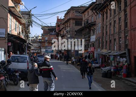 Bhaktapur, Kathmandu, Nepal - 23 dicembre 2019: Persone non identificate camminano per strada, moto e auto sono parcheggiate sul lato tra gli edifici Foto Stock