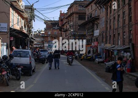 Bhaktapur, Kathmandu, Nepal - 23 dicembre 2019: Persone non identificate camminano per strada, moto e auto sono parcheggiate sul lato tra gli edifici Foto Stock