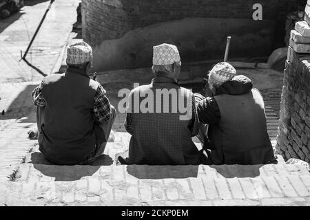 Bhaktapur, Kathmandu, Nepal - 23 dicembre 2019: Tre uomini non identificati si siedono e parlano sul lato della strada in alcune scale il 23 dicembre 2019 Foto Stock