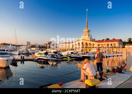 Sochi, Russia - 3 settembre 2020: I pescatori pescano il pesce nel porto sullo sfondo di yacht e barche al tramonto Foto Stock