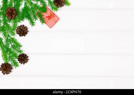 Rami dell'albero di Natale con coni di pino e scatola regalo rossa su tavole di legno bianche. Spazio di copia. Buon Natale sfondo Foto Stock