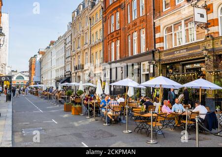 Al fresco lungo la strada per pranzo socializzare, cenare, mangiare e bere nella zona pedonale di Henrietta Street, Covent Garden, Londra WC2 in una giornata di sole Foto Stock