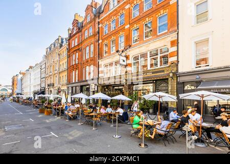 Al fresco lungo la strada per pranzo socializzare, cenare, mangiare e bere nella zona pedonale di Henrietta Street, Covent Garden, Londra WC2 in una giornata di sole Foto Stock