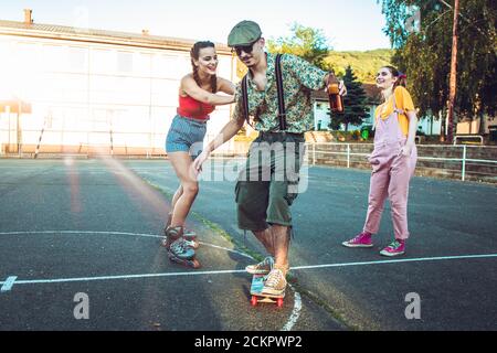 Ragazzo teenager sullo skate con due ragazze dietro di lui che si acclamano e ridendo Foto Stock