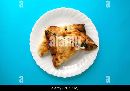 Famosa cucina tradizionale araba, mediorientale, israeliana. Spinaci Manakish su uno sfondo blu luminoso. Torta triangolare di spinaci su piatto bianco. Vista dall'alto Foto Stock