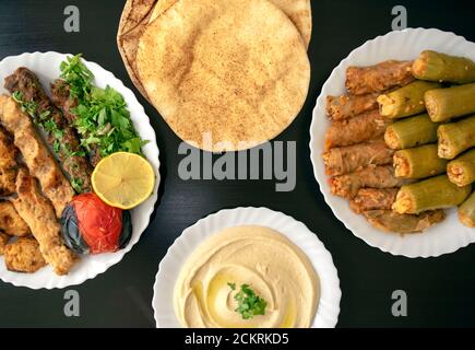 Famoso cibo tradizionale arabo, turco, israeliano. Pollo alla griglia, kofta kebab, mahshi, involtini di cavolo, pane pita, tahini su piatto bianco su legno scuro Foto Stock