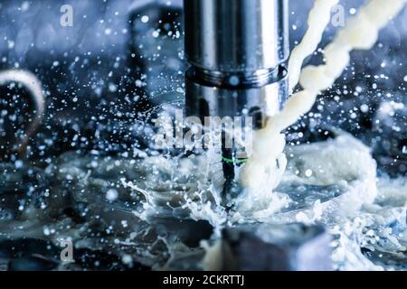 Vista ravvicinata del processo di fresatura verticale in acciaio cnc con flussi di liquido di raffreddamento dell'acqua esterni, schizzi e molti trucioli metallici, contrasto elevato Foto Stock