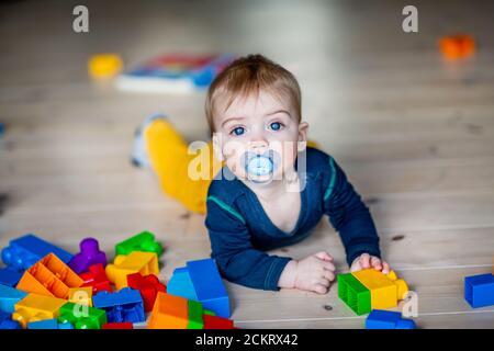 bambino di 6-9 mesi con un succhietto che gioca il pavimento Foto Stock