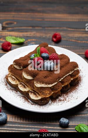 Porzione di tipico dessert tiramisù con lamponi e mirtilli sfondo di legno Foto Stock