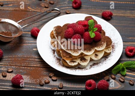 Porzione di tipico dessert tiramisù con lamponi su sfondo ligneo Foto Stock