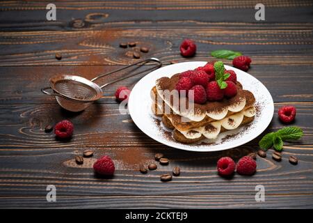 Porzione di tipico dessert tiramisù con lamponi su sfondo ligneo Foto Stock