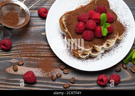 Porzione di tipico dessert tiramisù con lamponi su sfondo ligneo Foto Stock