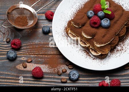 Porzione di tipico dessert tiramisù con lamponi e mirtilli sfondo di legno Foto Stock