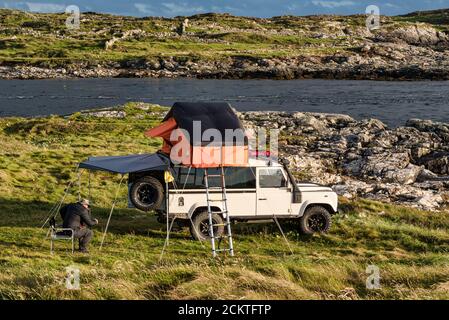 Clifden, Irlanda - 25 luglio 2020; un uomo che si accampano sulla costa occidentale dell'Irlanda in una Land Rover con una tenda sul tetto Foto Stock