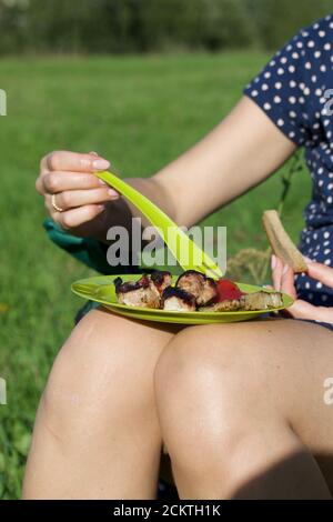 La ragazza mangia carne alla griglia. La carne è su un piatto. Piatto sul grembo della ragazza. Primo piano. Foto Stock