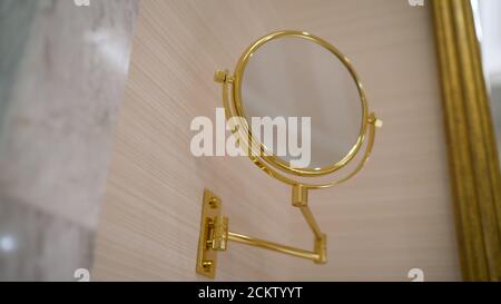 Nuovo bagno con carta da parati a motivi, pavimento scintillante, specchio rotondo con cornice dorata decorativa e lavandino nero. Uno specchio rotondo dorato nel bagno. Foto Stock