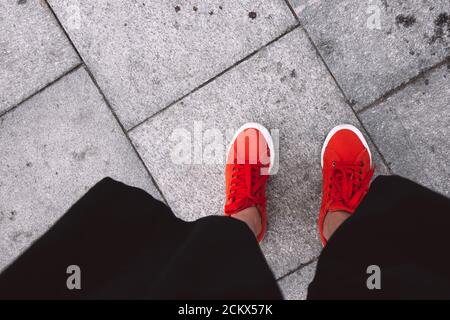 Piedi femmina visti dall'alto. Selfie per qualsiasi uso. Piede e gambe in sneaker rosse. Piede in piedi sulle piastrelle grigie. Con spazio per la copia. Piedi fuori Foto Stock