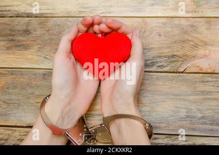 Mani femminili in manette tenendo un cuore rosso su sfondo di legno, spazio copia Foto Stock