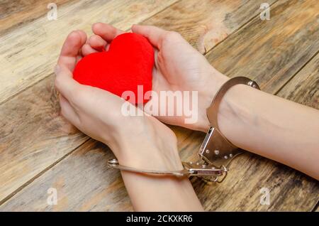 Mani femminili in manette tenendo un cuore rosso su sfondo di legno, spazio copia Foto Stock