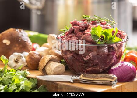 Carne di cervo a fette preparata per stufato di funghi di selvaggina erbe vegetali e coltello Foto Stock