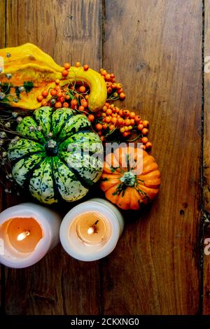 Composizione piatta in pumpkins, bacche di rowan e candele su tavola rustica in legno e sfondo nero. Verdure simboliche autunnali in verde Foto Stock