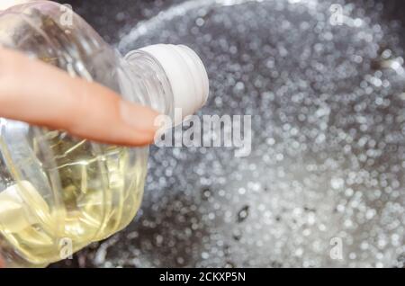 la mano della donna versa l'olio vegetale da una bottiglia su una padella da vicino, vista dall'alto Foto Stock