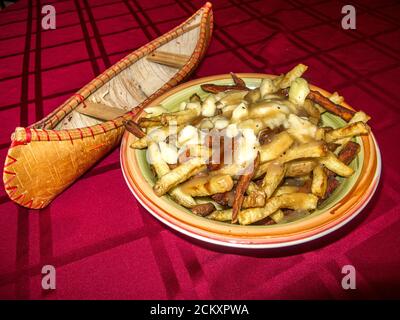 Poutine, un piatto di cibo francese canadese. Le patatine fritte sono ricoperte di salsa saporita e di curdi di formaggio. Accanto al piatto è un modello di una storica canoa con corteccia di betulla. Sun Peaks Resort, BC, Canada Foto Stock