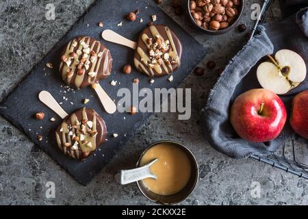 Popsicle di mele immerse nel cioccolato e nel caramello, costellato di nocciole tritate Foto Stock