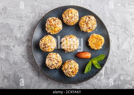 Torte Energy ball con albicocche secche, sesamo, lino, noci e datteri con foglie di menta verde su una piastra di ceramica blu su fondo grigio di cemento. Foto Stock