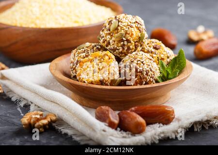 Torte di palla energetica con albicocche secche, sesamo, cornflakes, lino, noci e datteri con foglie di menta verde in una ciotola di legno su un dorso di cemento nero Foto Stock