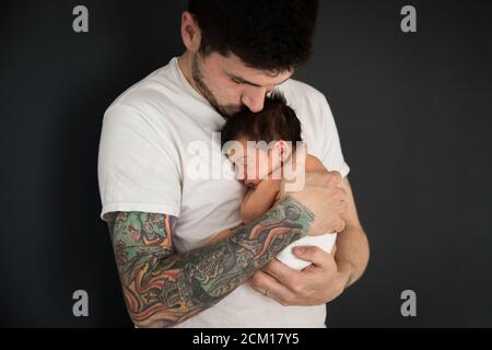 Tattooed Millennial Dad Kisses Newborn Son con pannolino Foto Stock