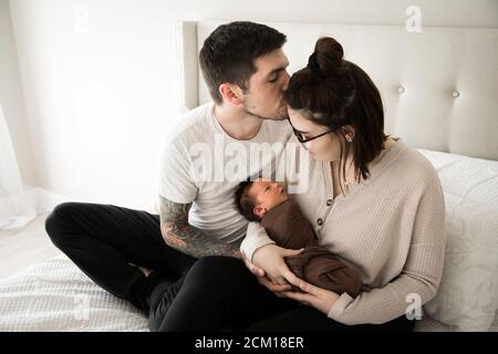 Tattooed Millennial Dad Kisses mamma mentre tiene il loro neonato Foto Stock