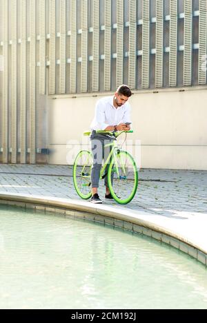 Outdoor ritratto del bel giovane con il telefono cellulare e il pignone fisso della bicicletta in strada. Foto Stock