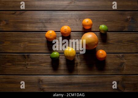 Agrumi freschi e maturi interi, come pompelmo, lime, limoni, arance e mandarini al centro su tavola di legno marrone. Vista dall'alto, spazio di copia. Foto Stock