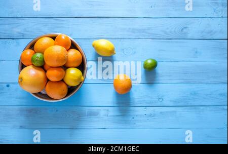 Mescolare gli agrumi interi maturi freschi come arance, mandarini, lime, pompelmo e limoni in una ciotola su uno sfondo di legno blu con copyspace, top Foto Stock