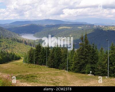 La pista sciistica di Marisel e il lago di Belis in estate nella giornata di sole, Romania. Appuseni scena montagne, Cluj contea, Transilvania, Romania. Pineta, bianco Foto Stock