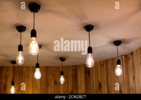 molte lampadine edison appese su un soffitto bianco in una stanza con pareti in legno, illuminazione elettrica in stile retrò in un ambiente eco-friendly interno primo piano di bagliore Foto Stock