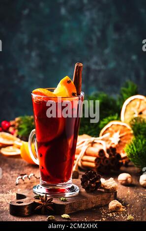 Vino rosso tritato natalizio con spezie e frutta in calice alto su tavola rustica in legno. Tradizionale bevanda calda di Natale in un ambiente da tavolo festivo Foto Stock