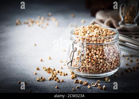 Groat di grano saraceno verde senza cottura in vaso di vetro, cibo vegetariano sano su tavolo da cucina grigio, spazio copia, fuoco selettivo Foto Stock