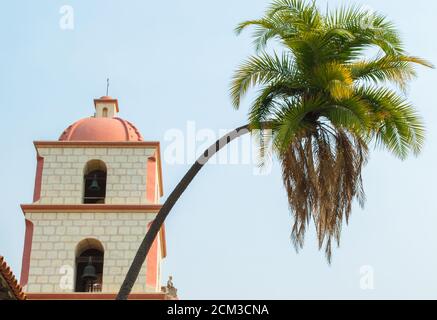 Una graziosa palma incurvata di fronte al campanile in stile spagnolo presso la storica missione di Santa Barbara in California sotto il sole frizzante Foto Stock