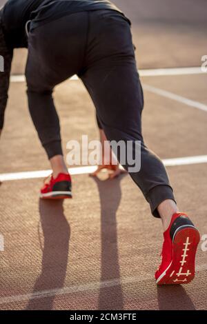 Vista posteriore dell'uomo in piedi in posizione di partenza per la corsa su pista in stadium Foto Stock