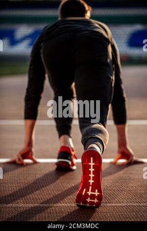 Vista posteriore dell'uomo in piedi in posizione di partenza per la corsa su pista in stadium Foto Stock