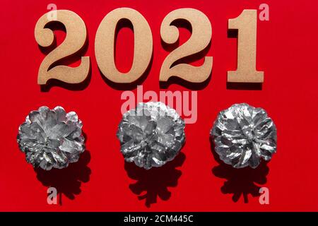 Fondo rosso di nuovo anno con numeri dorati lucenti 2021 e cono di pino argentato. Concetto minimalista su carta rossa con ombre dure. Foto Stock