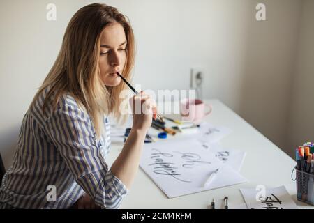 Ritratto dell'artista femminile di calligraphy pensa al lavoro mentre sedendo presso il banco dell'officina Foto Stock